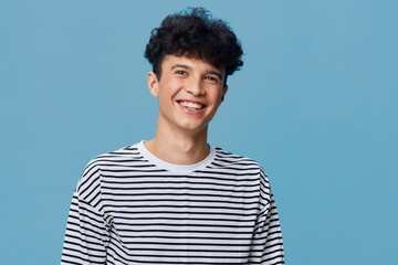 smiling man wearing striped shirt stands against solid blue background, joyful expression with...