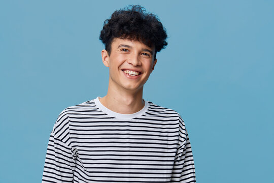 smiling man wearing striped shirt stands against solid blue background, joyful expression with curly hair, casual style portrait of young adult male