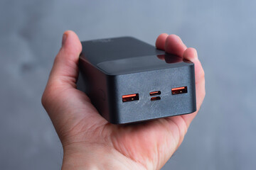 Close-up of a portable power bank held in hand with USB-A and USB-C ports. Powerbank for travel,...