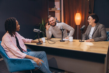 Three podcasters sitting at a desk and recording a show in a professional studio, talking and having fun