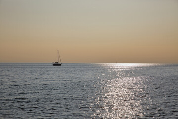 Sailboat silhouette on calm sea at golden hour sunset