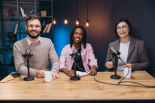 Podcasters discussing animatedly around studio table, holding microphones and coffee mugs during live recording session