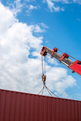 Red crane lifting red cargo container against sky and clouds