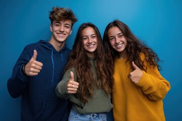 Teenage friends celebrating friendship with thumbs up in front of vibrant blue background during a casual gathering