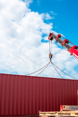 A red crane lifts a red cargo container, preparing for transportation