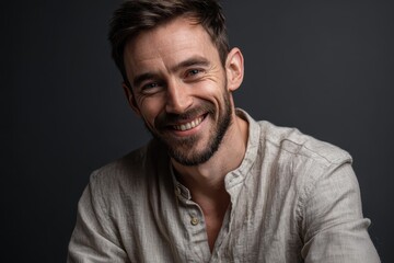 Obraz premium Smiling tall man in casual attire poses for a studio waistup shot against a dark backdrop during a portrait session