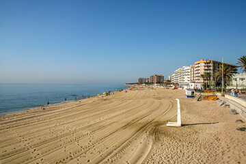 A city beach with high-rise buildings and calm seas under clear blue skies.