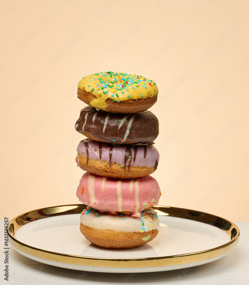 Poster stack of donuts with different toppings and glazes on round plate, beige background