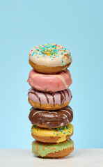 A tall stack of six colorful, glazed donuts with various toppings is centrally placed on a white...