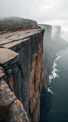 Towering sea cliffs stand majestically above the vast ocean, shrouded in atmospheric mist on a cloudy day, showcasing nature's immense power.