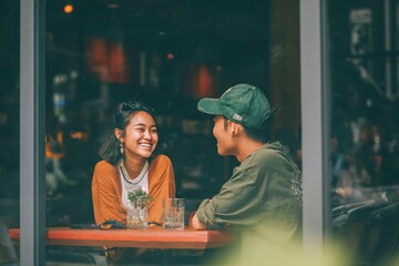 Happy Asian couple enjoying conversation in a cafe during the afternoon with laughter and smiles amidst a cozy atmosphere
