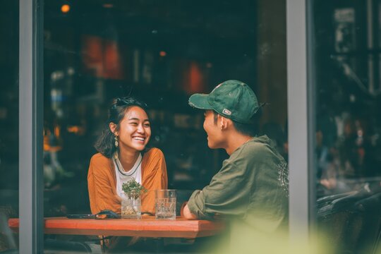 Happy Asian couple enjoying conversation in a cafe during the afternoon with laughter and smiles amidst a cozy atmosphere