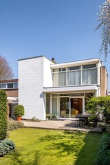 Fototapeta premium The contemporary architectural style of a stunning white house is enhanced by a generously sized garden and a charming outdoor dining area, all basking in the brilliance of a clear, sunny day