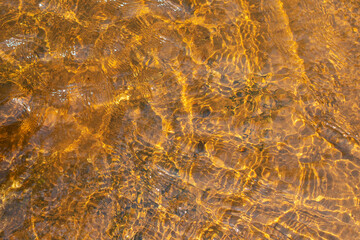 Shallow river water with ripples and sun glare on its surface. Abstract background texture