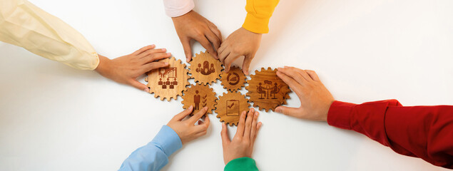 A vibrant display of diverse hands reaching for wooden gears, symbolizing teamwork and management...