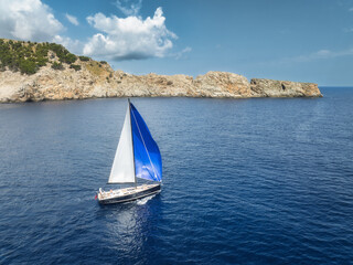 Aerial view of beautiful sailboat. Boat on the sea at sunset in summer. Top view of luxury yacht, sail boat, clear blue water, sky, mountain. Travel. Cruise vacation. Yachting. Balearic Islands, Spain