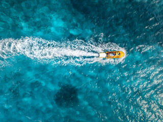 Aerial view of a yellow jetski sailing fast on turquoise water in Mallorca, Balearic Islands, Spain. Summer travel. Top drone view of speed boat, blue sea. Tropical seascape.