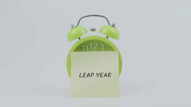 Leap year word on sticky note in front of green clock and ringing on white background, symbolizing calendar events, rare dates, and time awareness