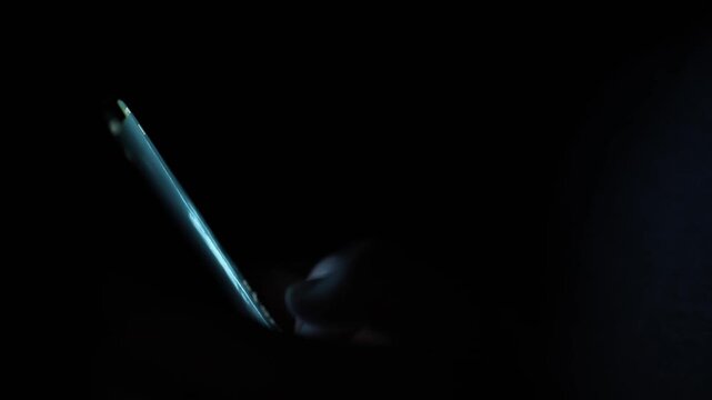 Fingers glow faintly as they tap a smartphone screen in near-total darkness capturing a secretive late-night texting moment filled with isolation tension and digital obsession