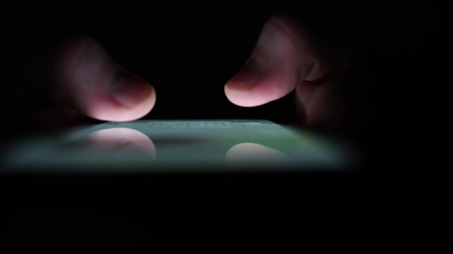 Extreme closeup of fingertips glowing over a smartphone screen in darkness symbolizing late night scrolling obsession social media addiction and isolation in digital age minimalism