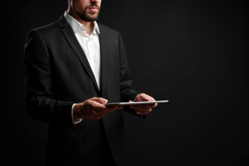 Professional man in formal attire holding a tablet in a dark setting during a business presentation