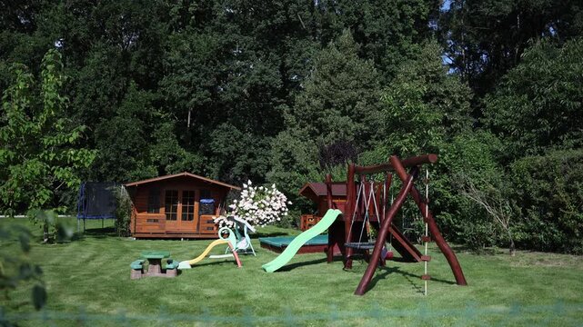 Sunny backyard playground with wooden swings slide trampoline and playhouse surrounded by lush greenery and trees creating a cheerful and safe outdoor space for kids to enjoy summer