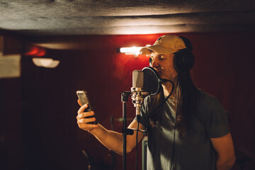 Singer recording song reading lyrics from smartphone in recording studio