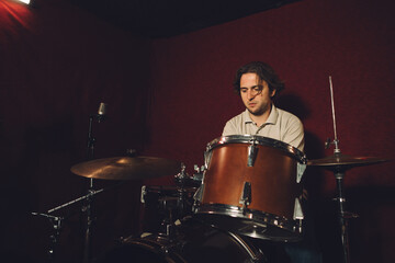 Drummer playing drums in recording studio with red background