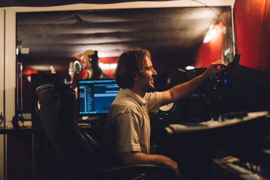 Sound engineer mixing music while singer recording song in studio - Powered by Adobe