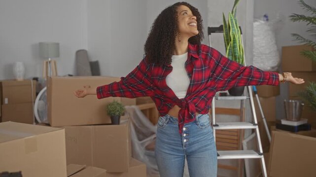 Woman with arms crossed in office filled with packed cardboard boxes, ladder and potted plants; hopefulness.