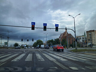 A busy urban intersection in Szczecin, Poland, under a cloudy sky, featuring traffic lights, a...