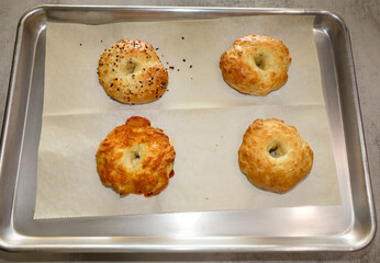 Four homemade freshly make bagels on a baking sheet.