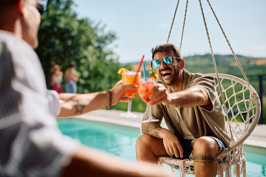 Cheerful friends toasting with summer cocktails at pool party.