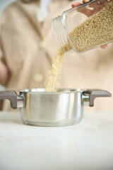 A girl pours white rice from a glass jar into a metal pot