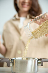 A girl pours white rice from a glass jar into a metal pot