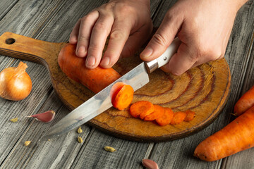 Hands skillfully slice vibrant carrots on a wooden cutting board. Nearby, onions and garlic add color to the inviting kitchen atmosphere during meal preparation