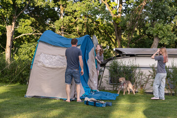 Family members are setting up a camping tent in a lush green backyard, enjoying outdoor activities and creating memorable experiences together
