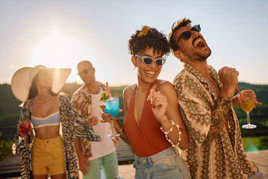 Young cheerful friends dancing while drinking cocktails at summer party. - Powered by Adobe