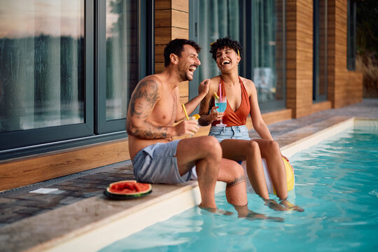Carefree couple having fun while drinking cocktails at poolside during summer.