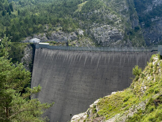 Vajont Dam. Massive concrete dam surrounded by lush green mountains and rocky terrain, showcasing engineering marvel and natural beauty in harmony