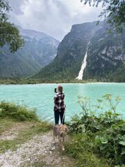 Durrensee. Woman with dog is taking a photo by a turquoise lake surrounded by mountains and lush greenery, capturing a serene outdoor moment