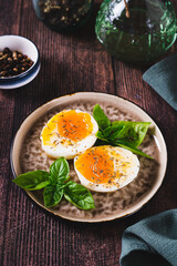 Spicy soft-boiled egg halves and basil on a plate on a table vertical view