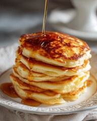 Stack of fluffy pancakes with maple syrup drizzle on white plate