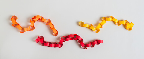 Three colored handmade paper chains on a light background top view
