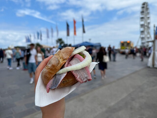 Traditional north german street food snack wheat bun with marinated herring matjes fish with onion in female hand close up
