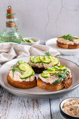 Appetizing sandwiches with cod liver pate, cucumber and arugula on a plate vertical view