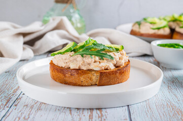 Cod liver, cucumber slices and arugula crostini on a plate on a table