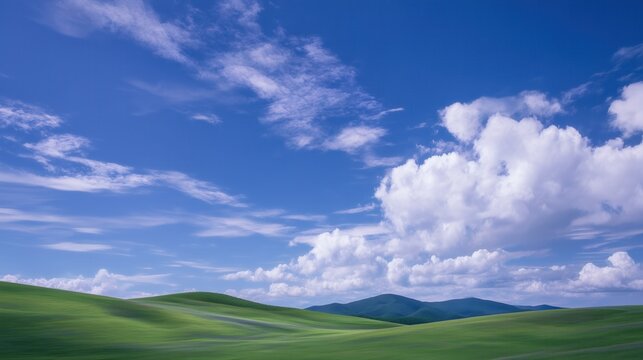 Idyllic landscape featuring vibrant green rolling hills under a clear blue sky dotted with fluffy white clouds, creating a serene and picturesque scene