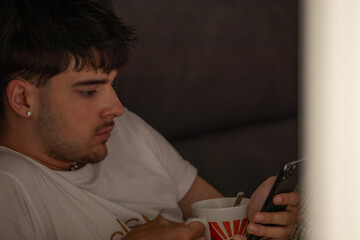 young man with mobile phone or smartphone at home on the sofa