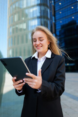 Business professional smiles while using tablet in modern cityscape at sunny day